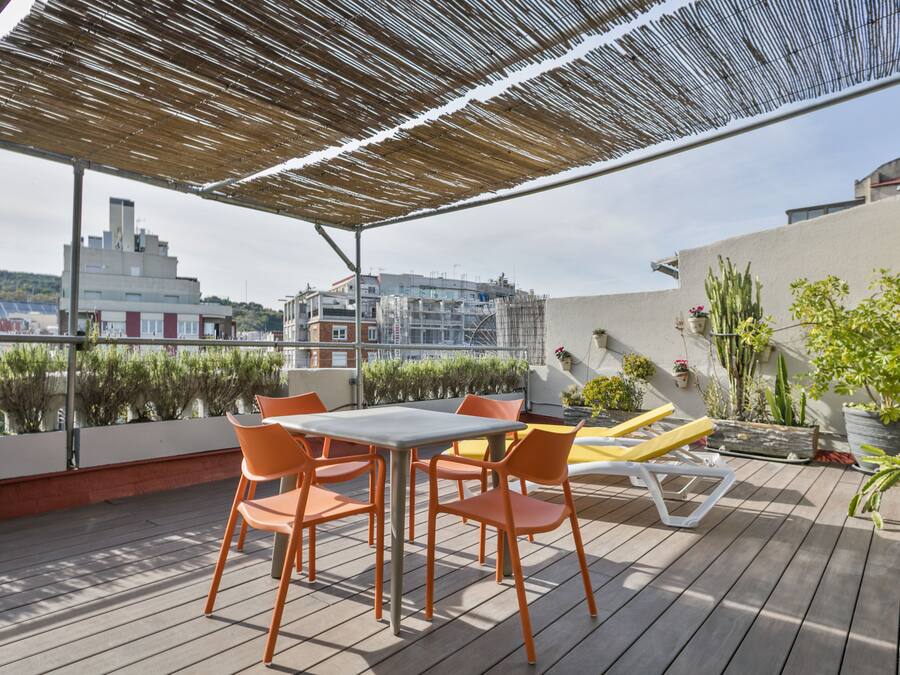 A rooftop terrace with a table and chairs, a sun lounger, and potted plants.