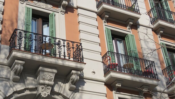 Fachada de edifício com varandas elaboradas, persianas verdes e detalhes arquitetônicos clássicos.