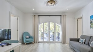 Uma sala de estar moderna com televisão de tela plana, poltronas azul-turquesa, um sofá cinza e uma grande janela com cortinas.
