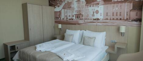 A hotel room with a large bed, a wardrobe, a desk, and a wall-mounted lamp.