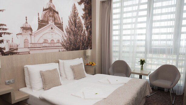 A hotel room with a large bed, two chairs, a small table, and a wall mural. - Košice Hotel (Kosice)