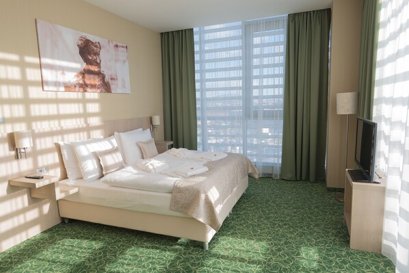 A hotel room with a large bed, a television, and a view of a cityscape through the window. - Košice Hotel (Kosice)