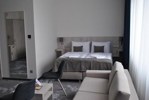A modern hotel room with a bed, a sofa, a chair, and a desk.