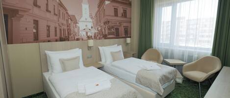 Une chambre d’hôtel avec deux lits, un bureau, une chaise, une grande fenêtre avec des rideaux et une fresque murale représentant un bâtiment.