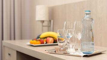 A hotel room with a wooden counter, two glasses, a bottle of water, and a fruit plate with bananas and apples.