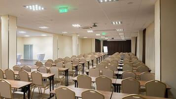 A conference room with rows of tables and chairs, a projector screen, and a stage at the front.