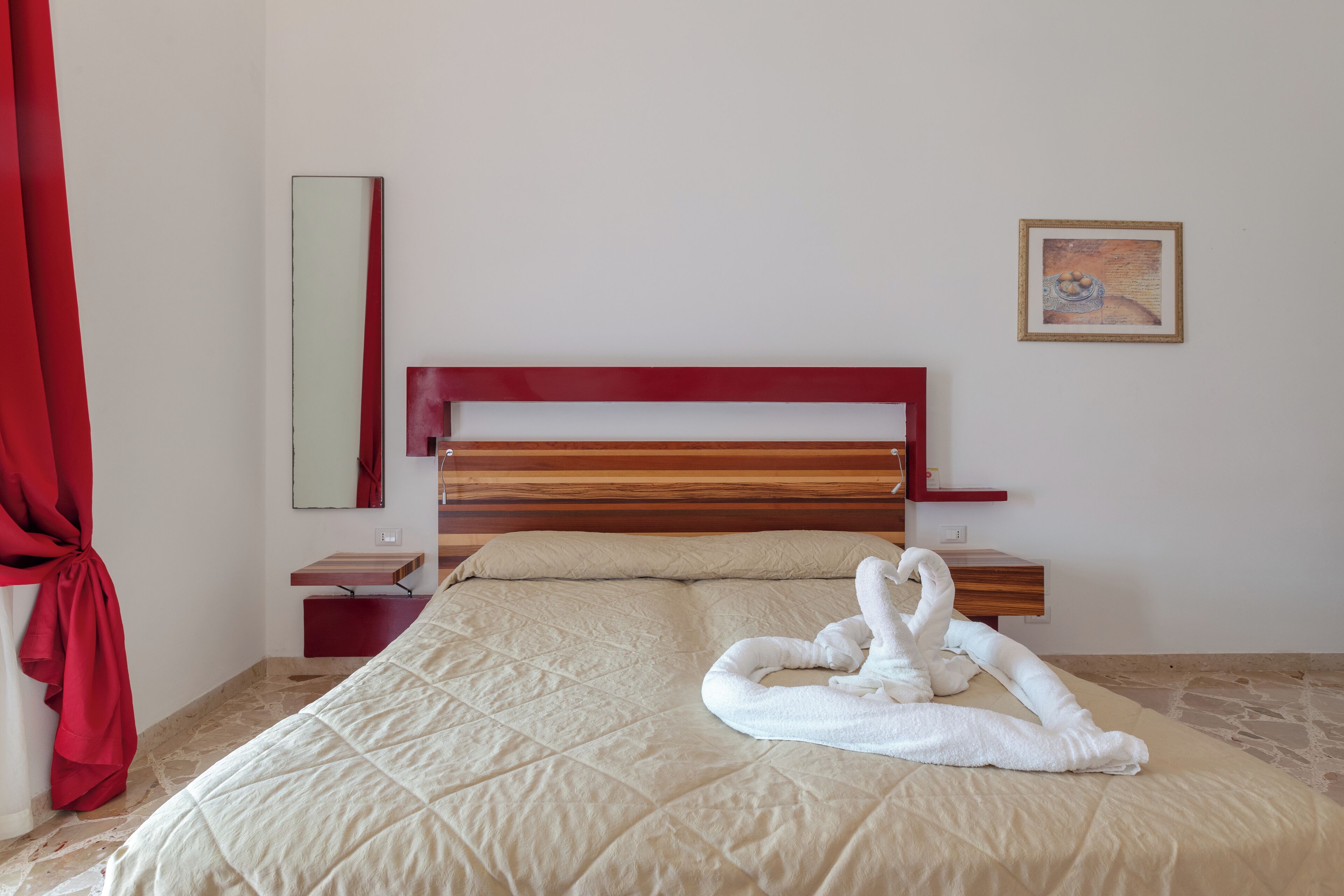 Una habitación de hotel con una cama, una mesita de noche, un espejo, una cortina roja y un cuadro en la pared.