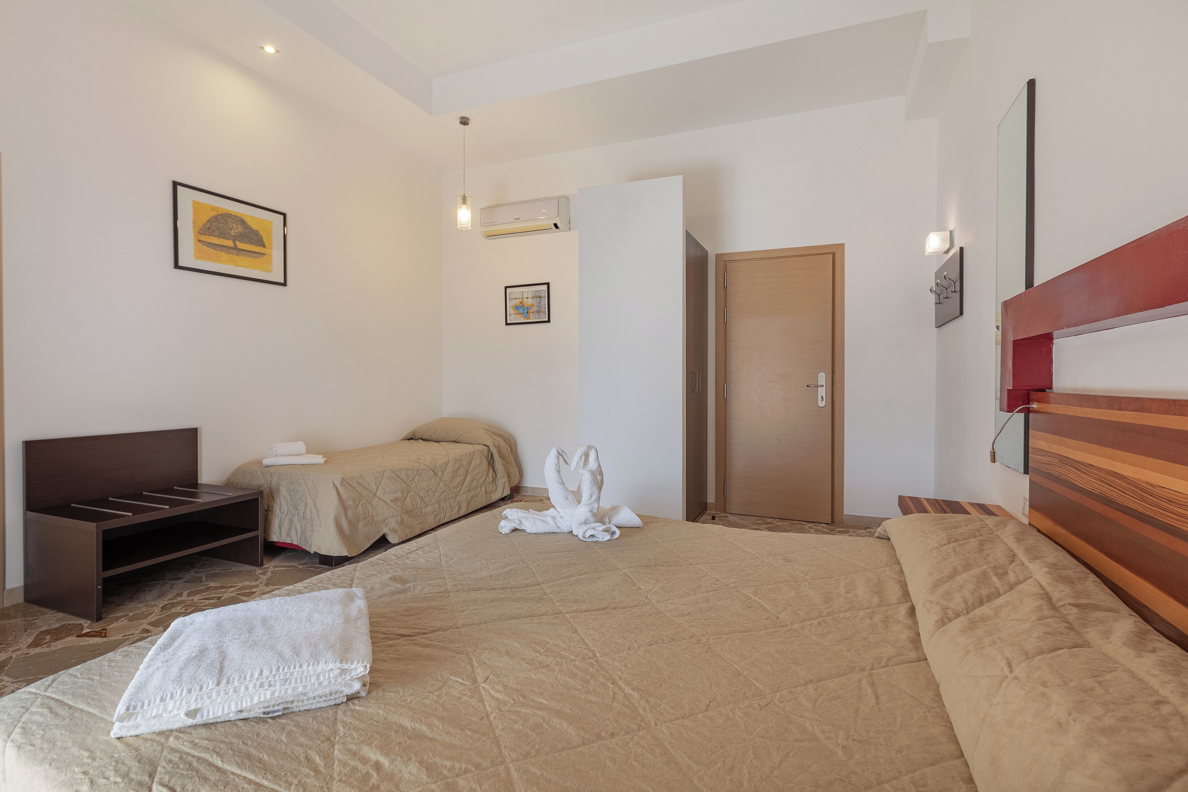 A hotel room with a large bed, a wooden headboard, a bedside table, a wardrobe, and a wall-mounted air conditioner.
