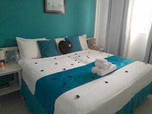 Quarto de hotel com cama, mesa de cabeceira, luminária e um quadro na parede.