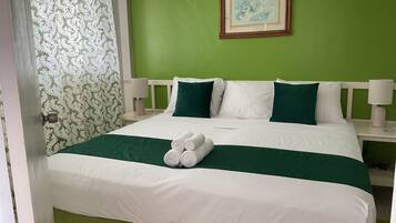 A neatly made bed with white and green bedding, a framed picture on the wall, and a patterned curtain.