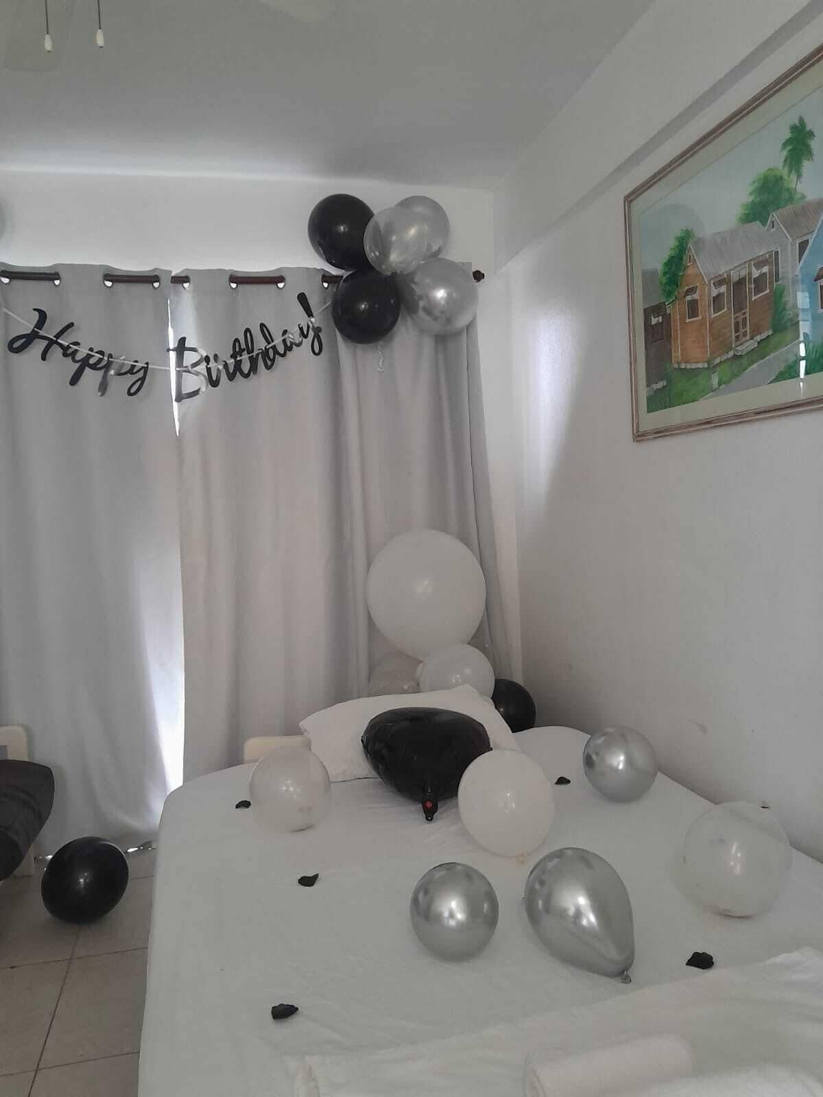 Un dormitorio con una cama, un cartel de 'Feliz Cumpleaños' y globos.