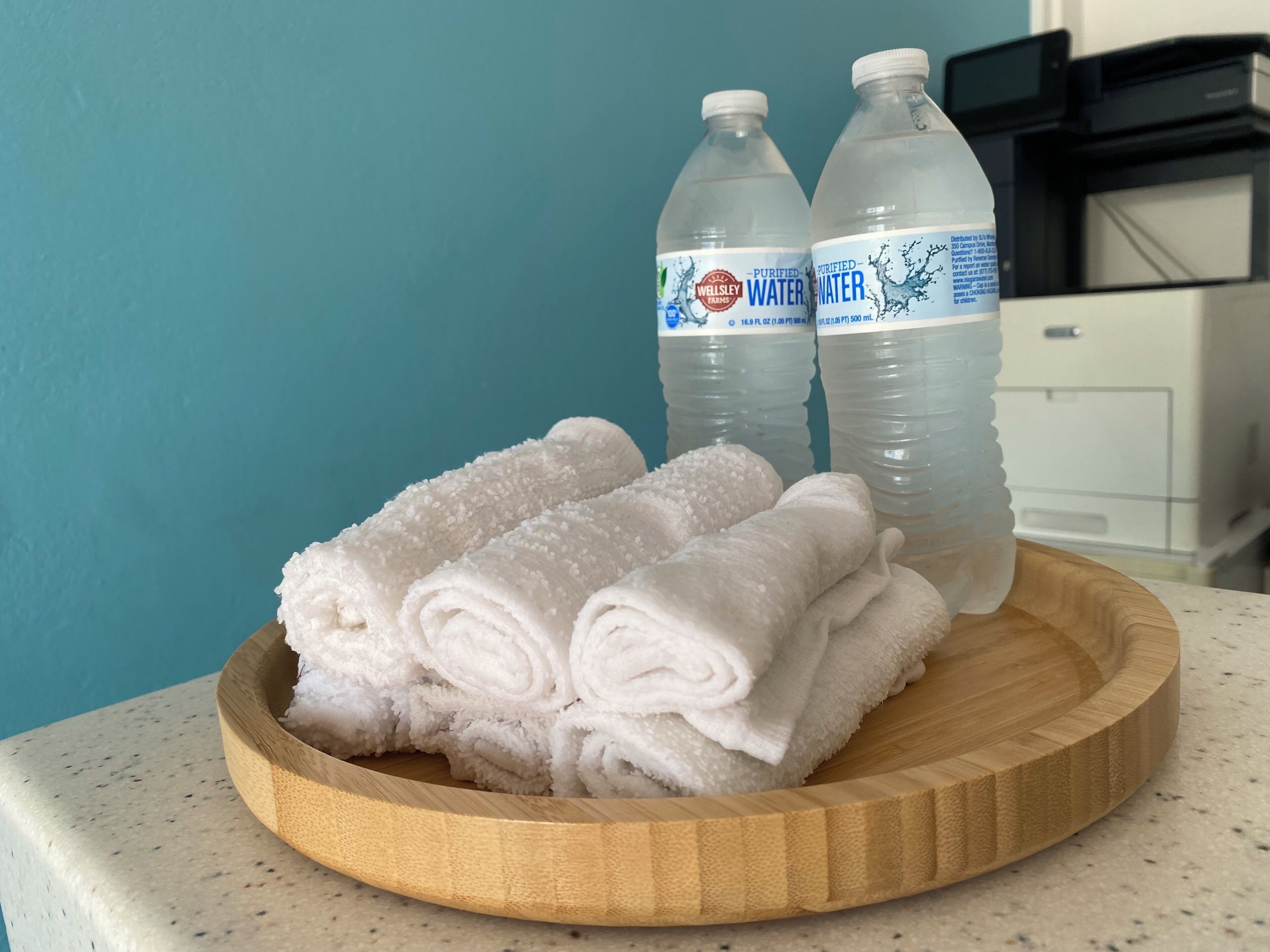 A wooden tray with rolled white towels and two bottles of purified water.