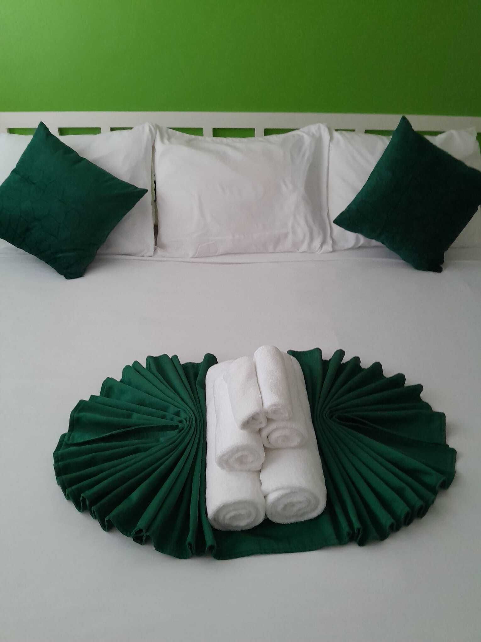 Un lit avec une literie blanche, deux oreillers verts et un coussin décoratif vert posé sur une tête de lit blanche.