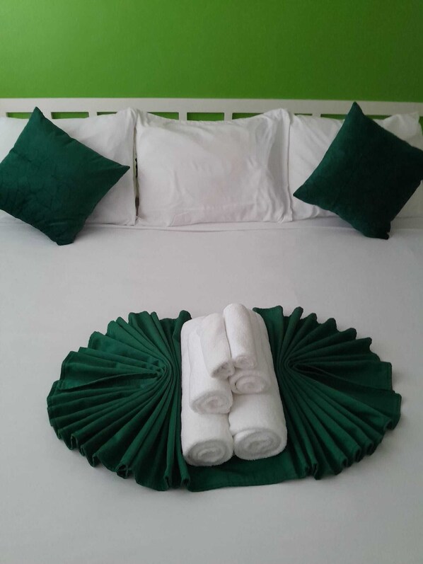 A bed with white bedding, two green pillows, and a green decorative pillow on a white headboard.