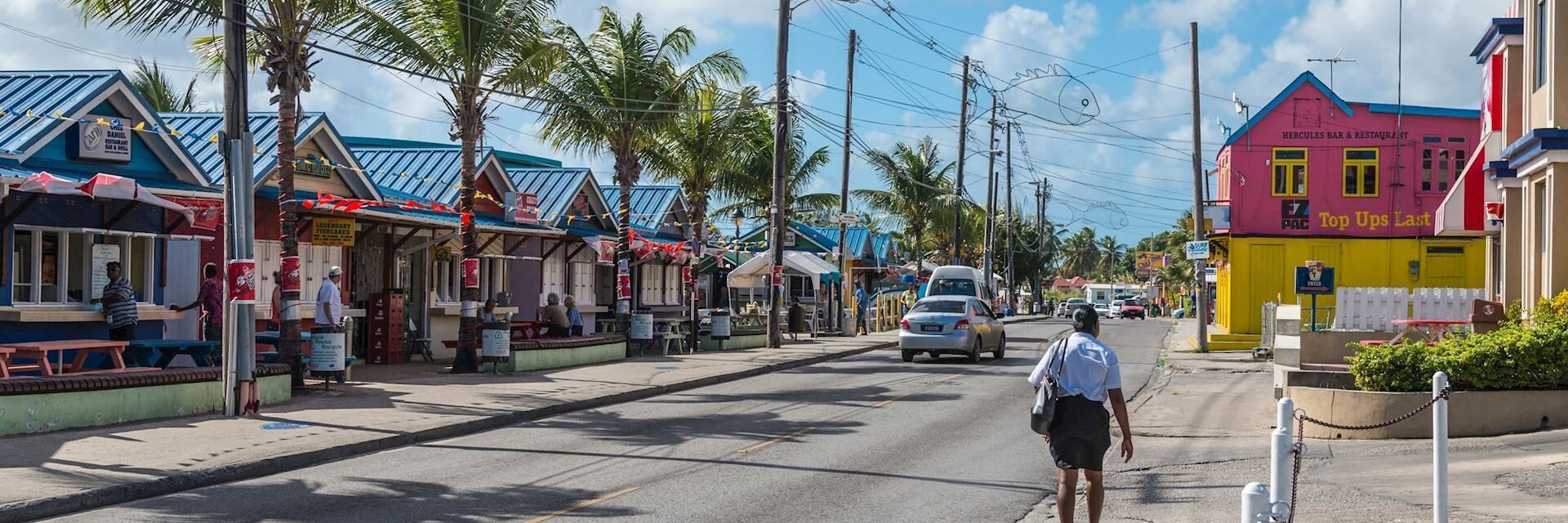 A street lined with colorful buildings, including a pink and yellow one with a sign for 'Top Ups Last'.