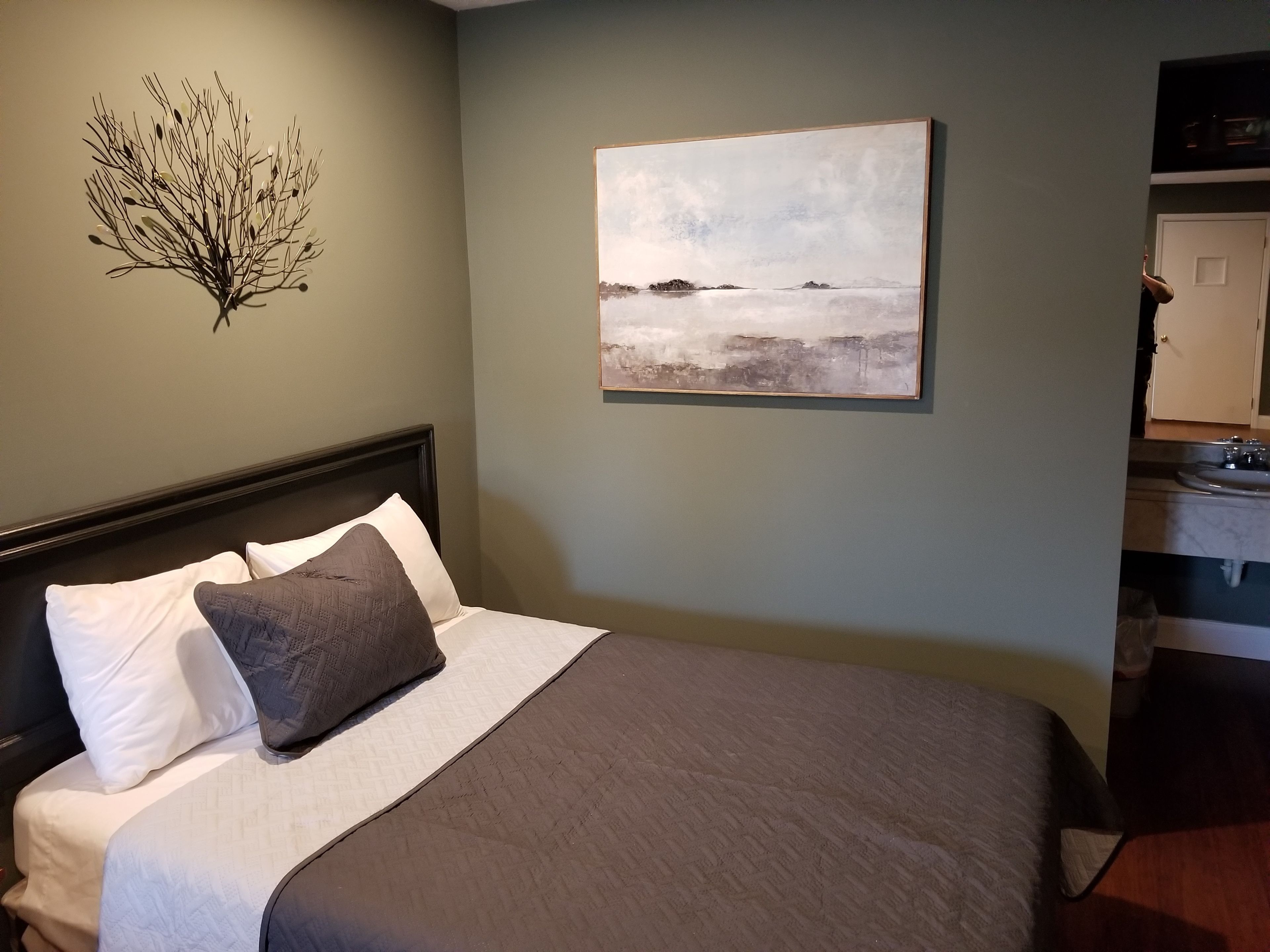 Una cama bien hecha con cabecera, un cuadro abstracto en la pared y una pequeña planta decorativa.