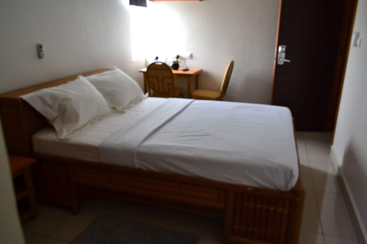 A single bed with a wooden frame, white bedding, and a small bedside table with a lamp.