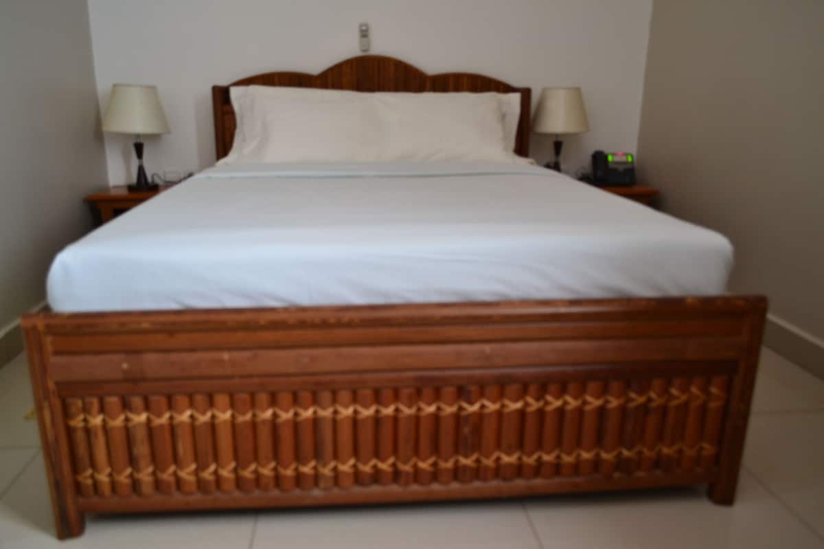 A standard hotel room with a wooden bed, two bedside tables with lamps, and a nightstand with a clock.