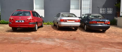 Three cars parked in front of a building with a grey facade and white windows.