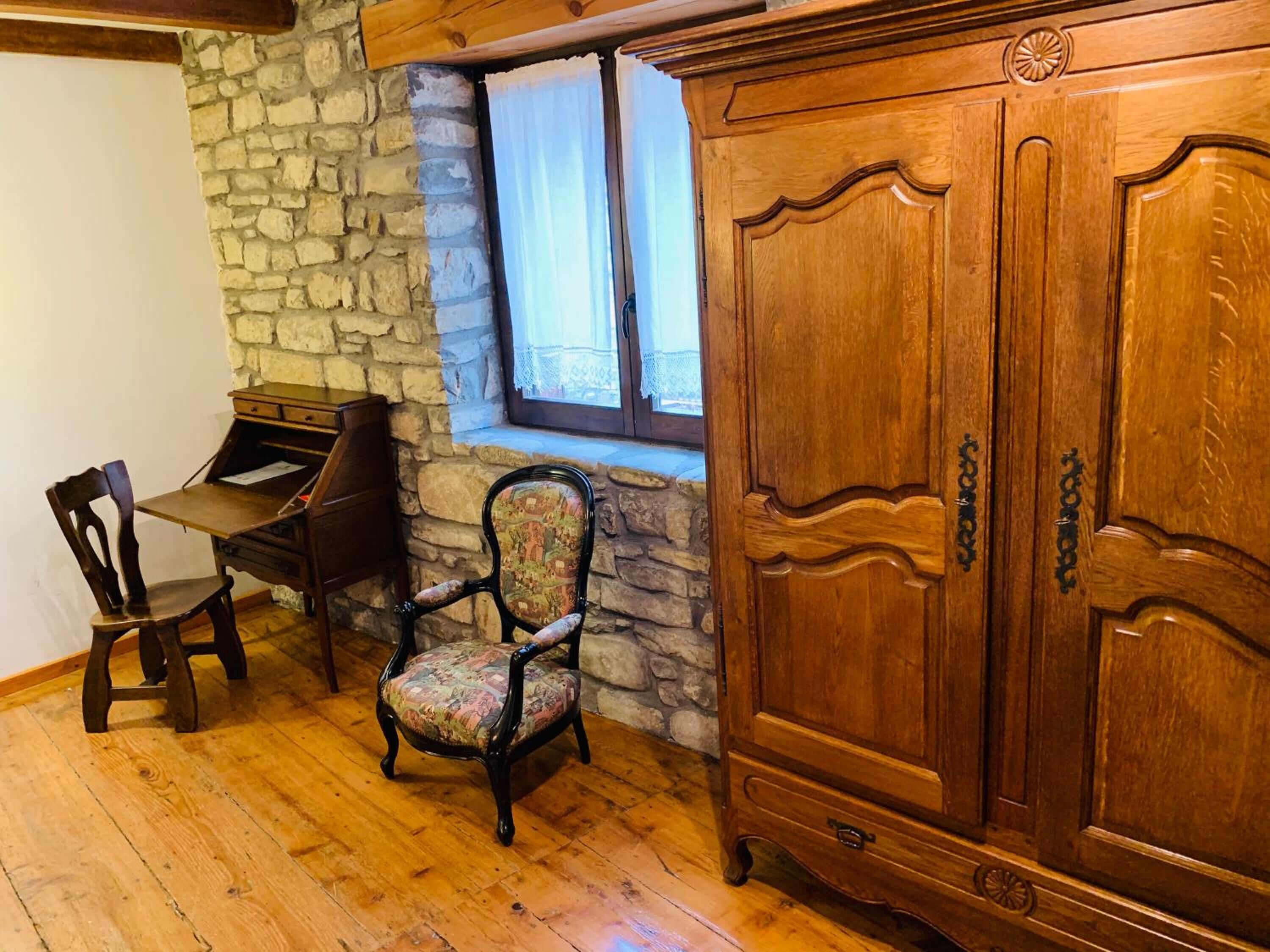 A room with a stone wall, wooden furniture, a window with curtains, and a wooden cabinet.