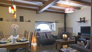 A cozy living room with a fireplace, a dining area with a table set for breakfast, and a comfortable seating area with a sofa and a TV. - Casa Rural Argonz Etxea (Urzainqui)