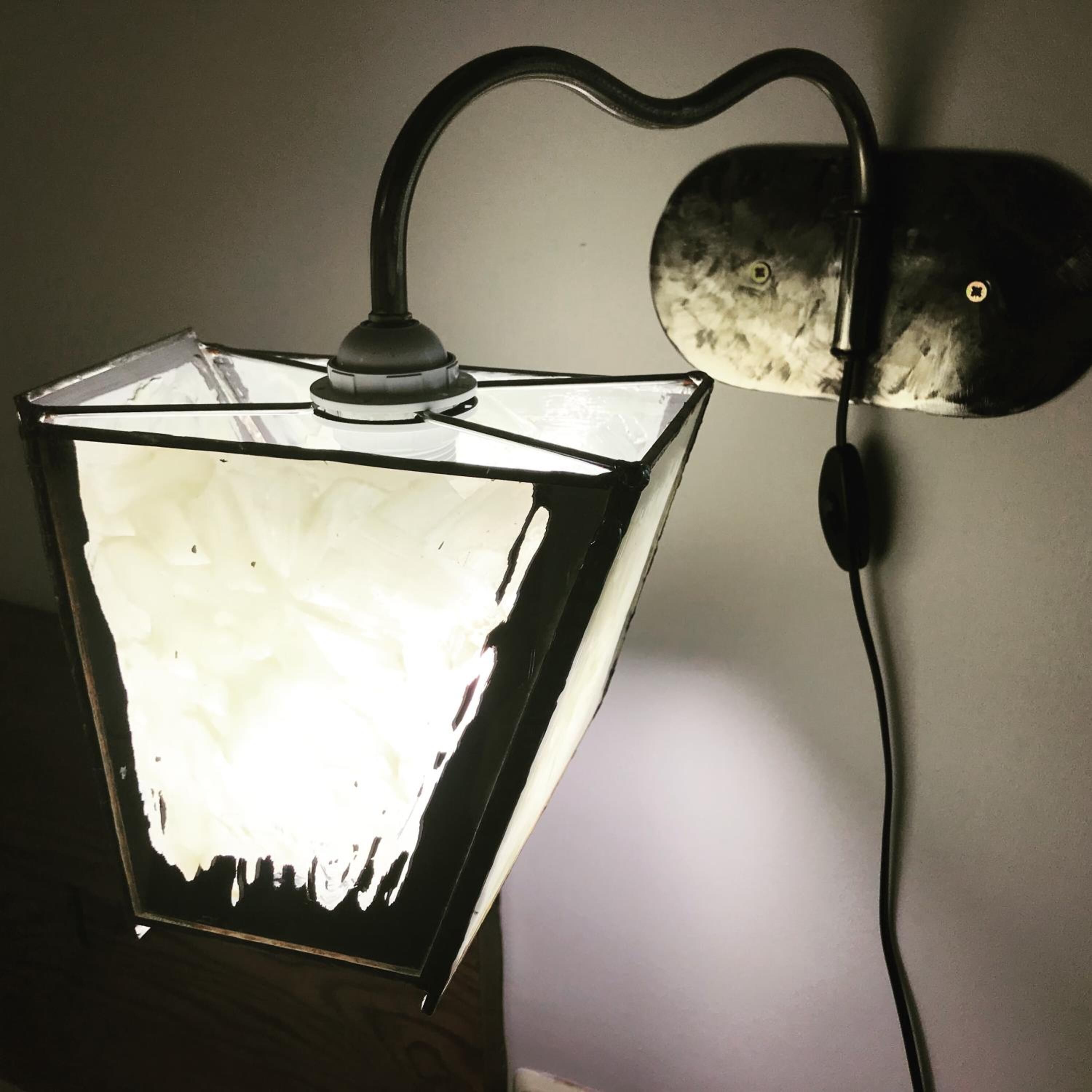 A square-shaped light fixture with a white, textured surface and a black cord connected to a wall-mounted switch.