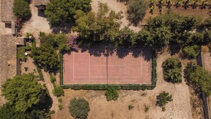 Vista aérea de una cancha de tenis rodeada de árboles y un edificio de piedra.