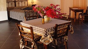Un comedor acogedor con una mesa lista para dos, una cama con cabecera de metal y una ventana con cortinas traslúcidas.
