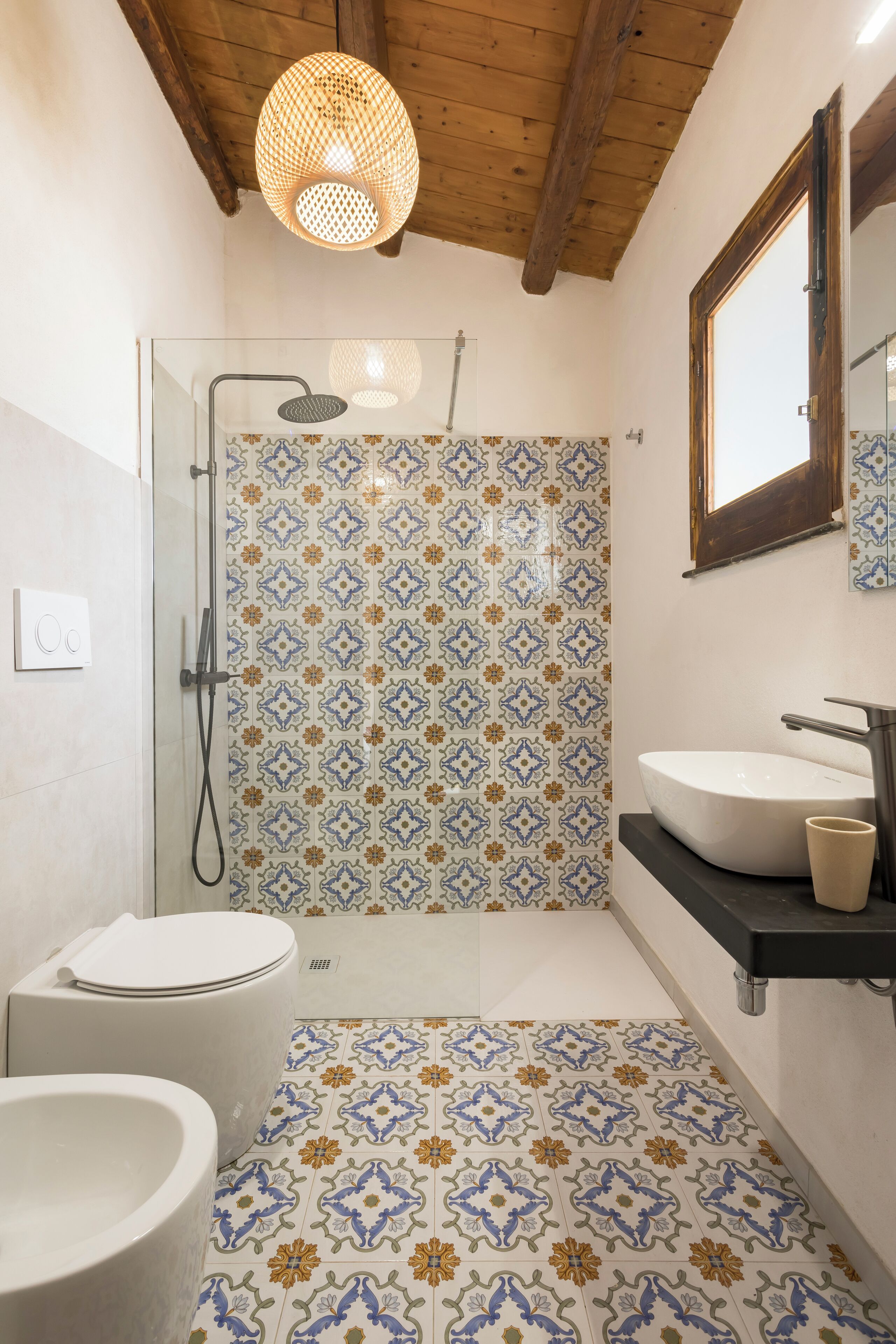 Ein Badezimmer mit Dusche, Toilette und Waschbecken, ausgestattet mit gemusterten Fliesen und Holzbalken.