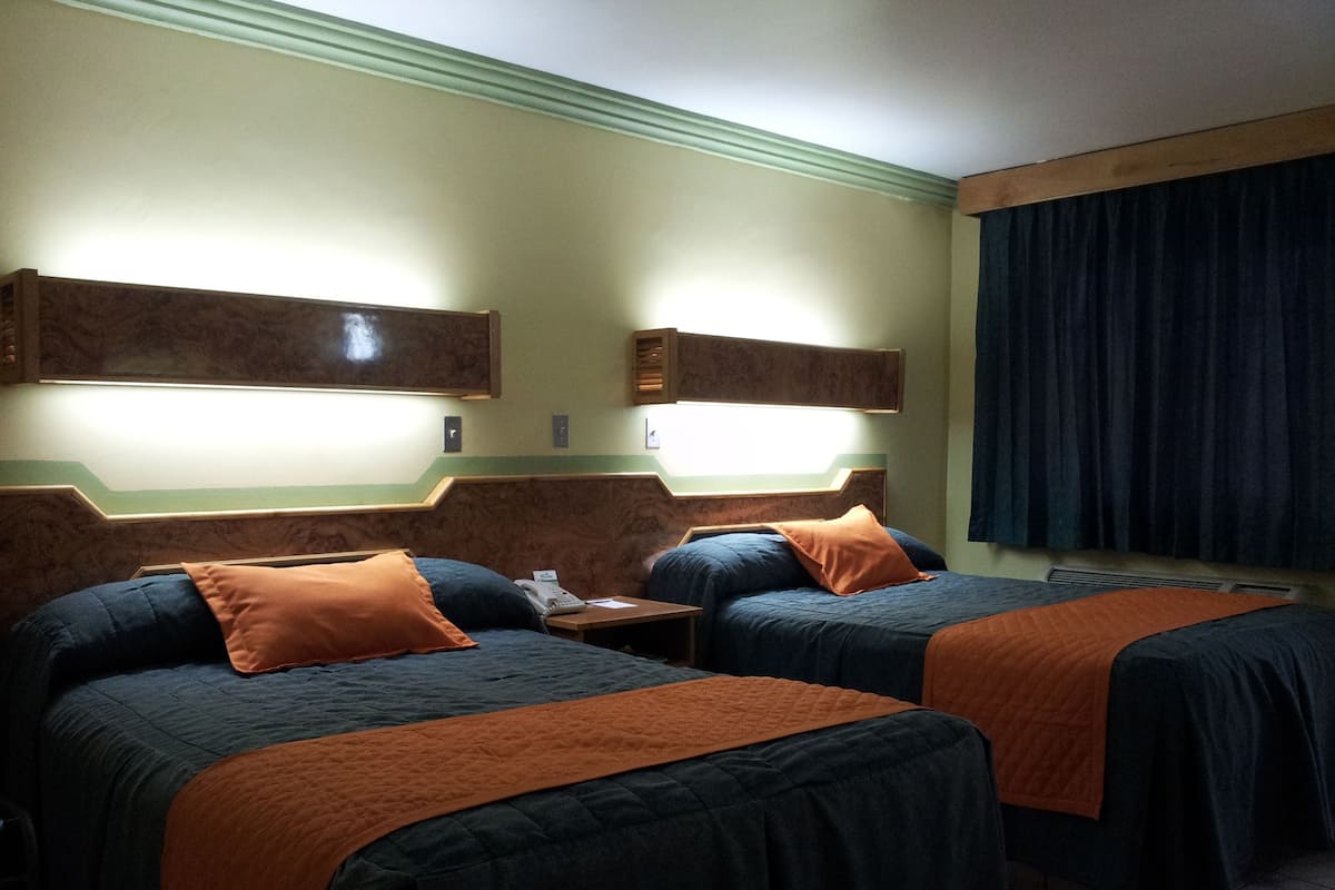 A hotel room with two beds, a nightstand, a telephone, and a window with curtains.