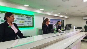 A reception desk with a glass partition, a digital welcome screen displaying multiple languages, and a clean, modern interior with a tiled floor. - Hotel Marques De Cima (Nogales)