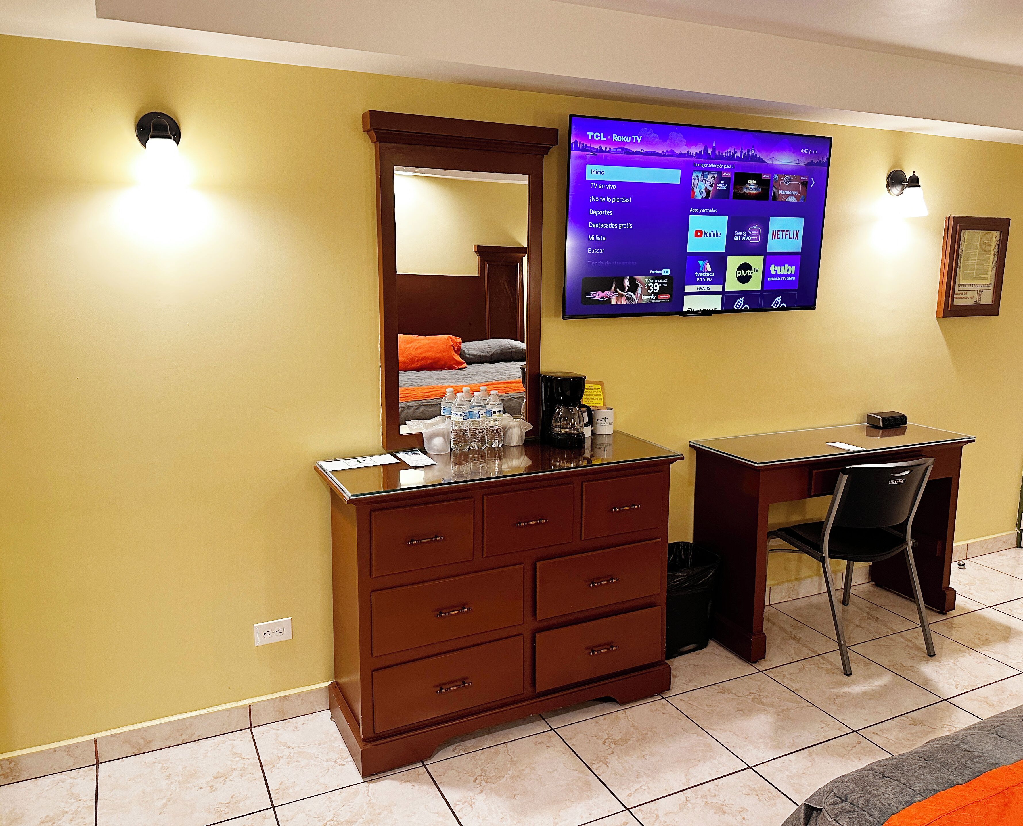 Quarto de hotel com televisão de tela plana na parede, cômoda de madeira, escrivaninha e uma cadeira.
