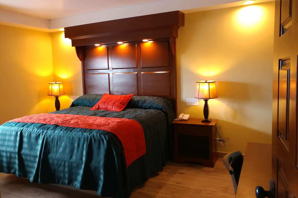 A hotel room with a large bed, two bedside tables with lamps, a wooden headboard, and a wooden door.