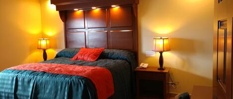 A hotel room with a large bed, two bedside tables with lamps, a wooden headboard, and a wooden door.