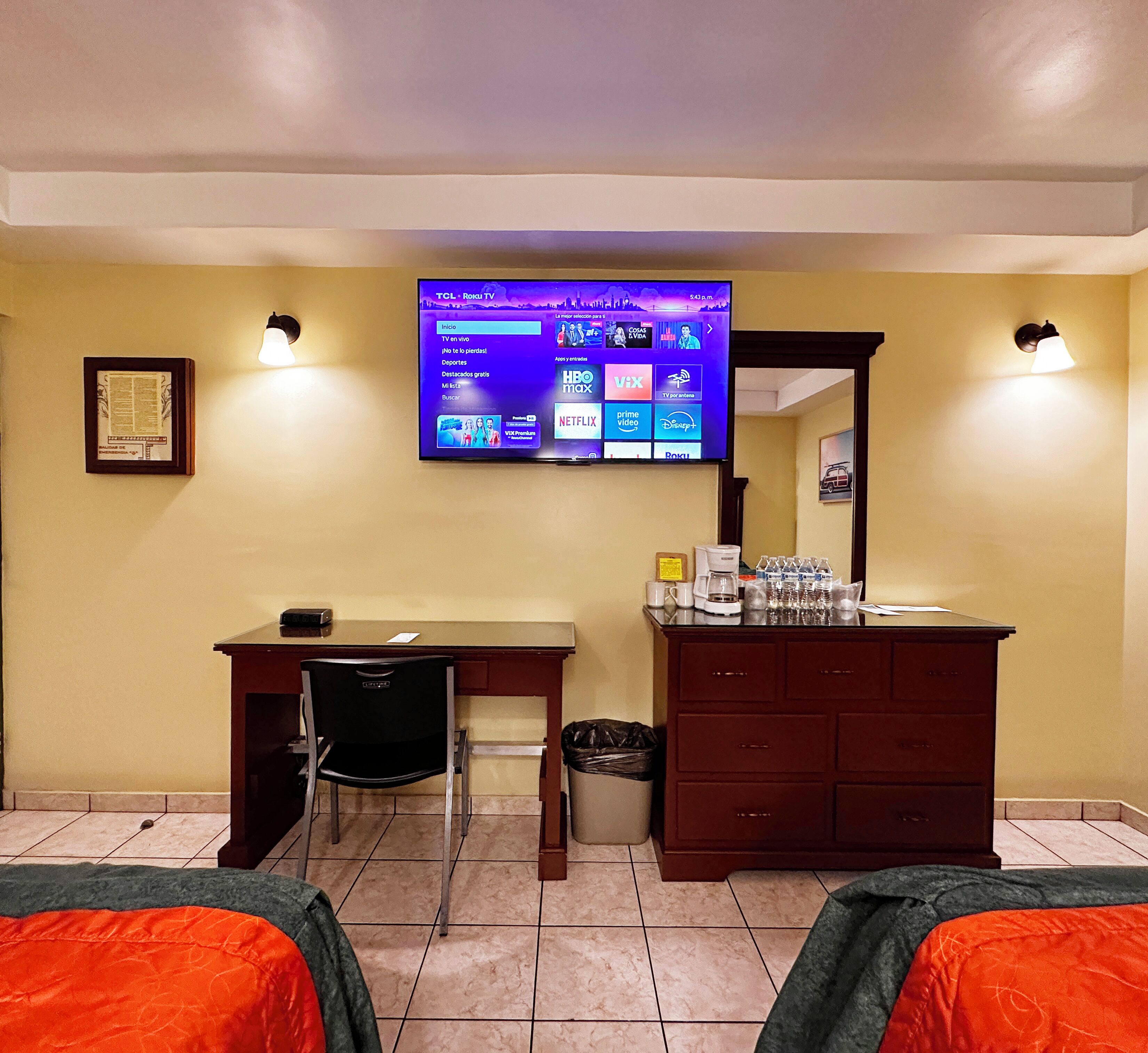 A hotel room with a bed, a desk, a chair, a TV mounted on the wall, and a small trash bin.
