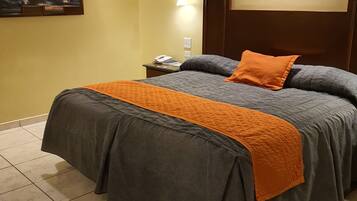 A hotel room with a bed, a nightstand, a wall-mounted lamp, and a painting.