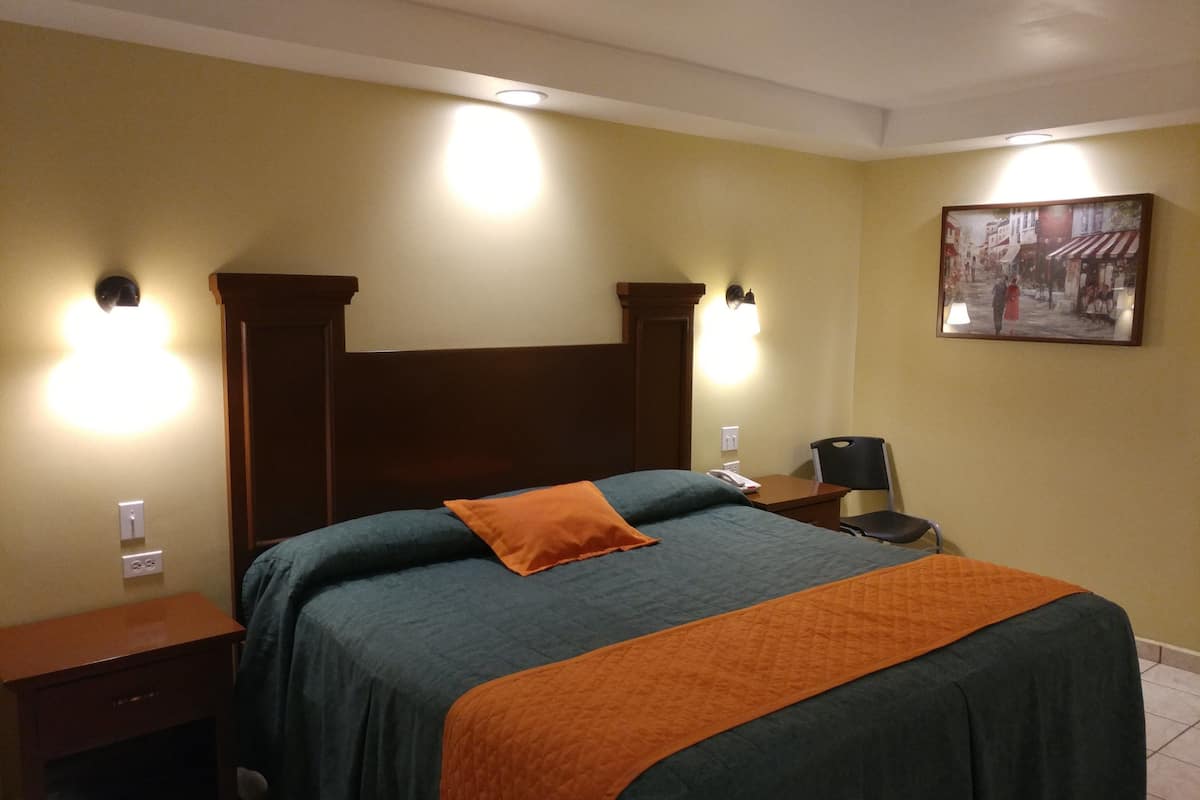 A hotel room with a large bed, two bedside tables, a nightstand, a chair, and a painting on the wall.