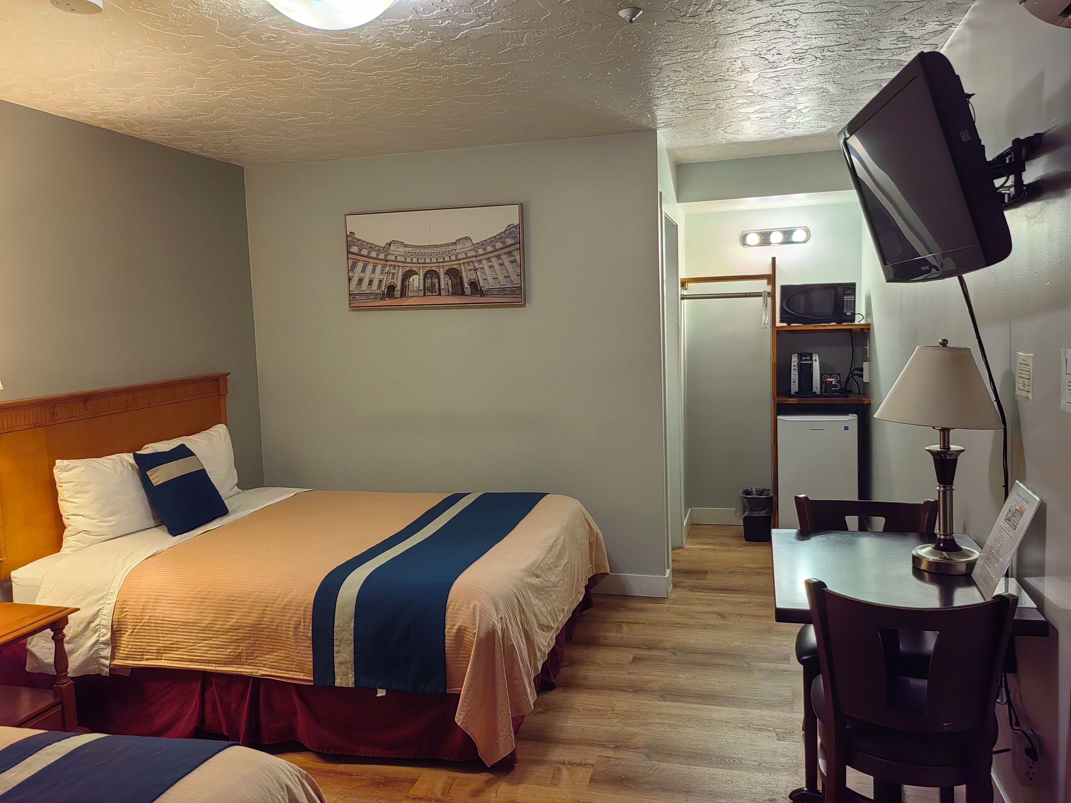 A hotel room with a bed, a desk with a chair, a television, and a picture of a building on the wall.