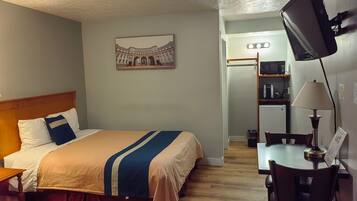 A hotel room with a bed, a desk with a chair, a television, and a picture of a building on the wall.