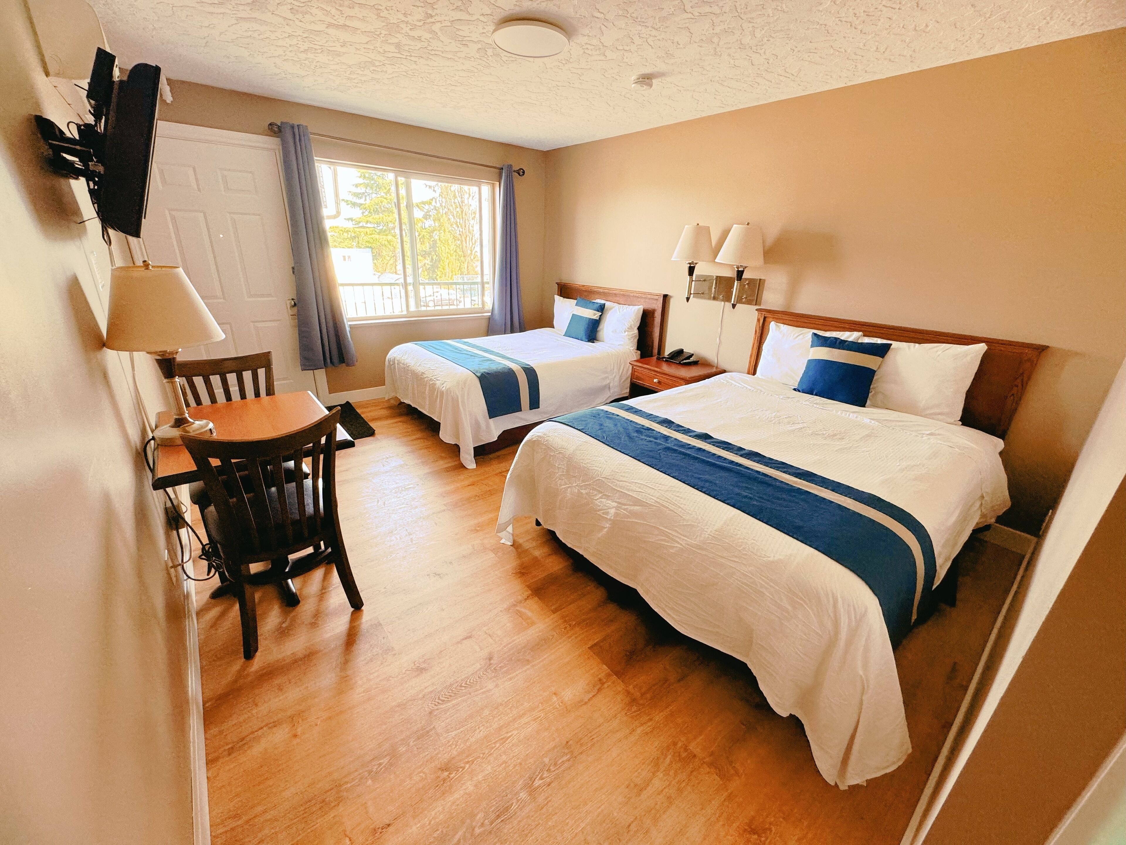 Une chambre d’hôtel avec deux lits, un bureau, une chaise, une fenêtre avec des rideaux et un luminaire au plafond.