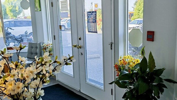 Zona de recepción de hotel con entrada por puerta de cristal, un reloj y un cartel que indica el horario de atención.