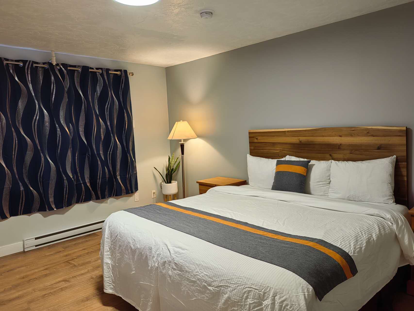 A neatly made bed with a white and gray striped bedspread, a wooden headboard, and two pillows with a gray and orange stripe.