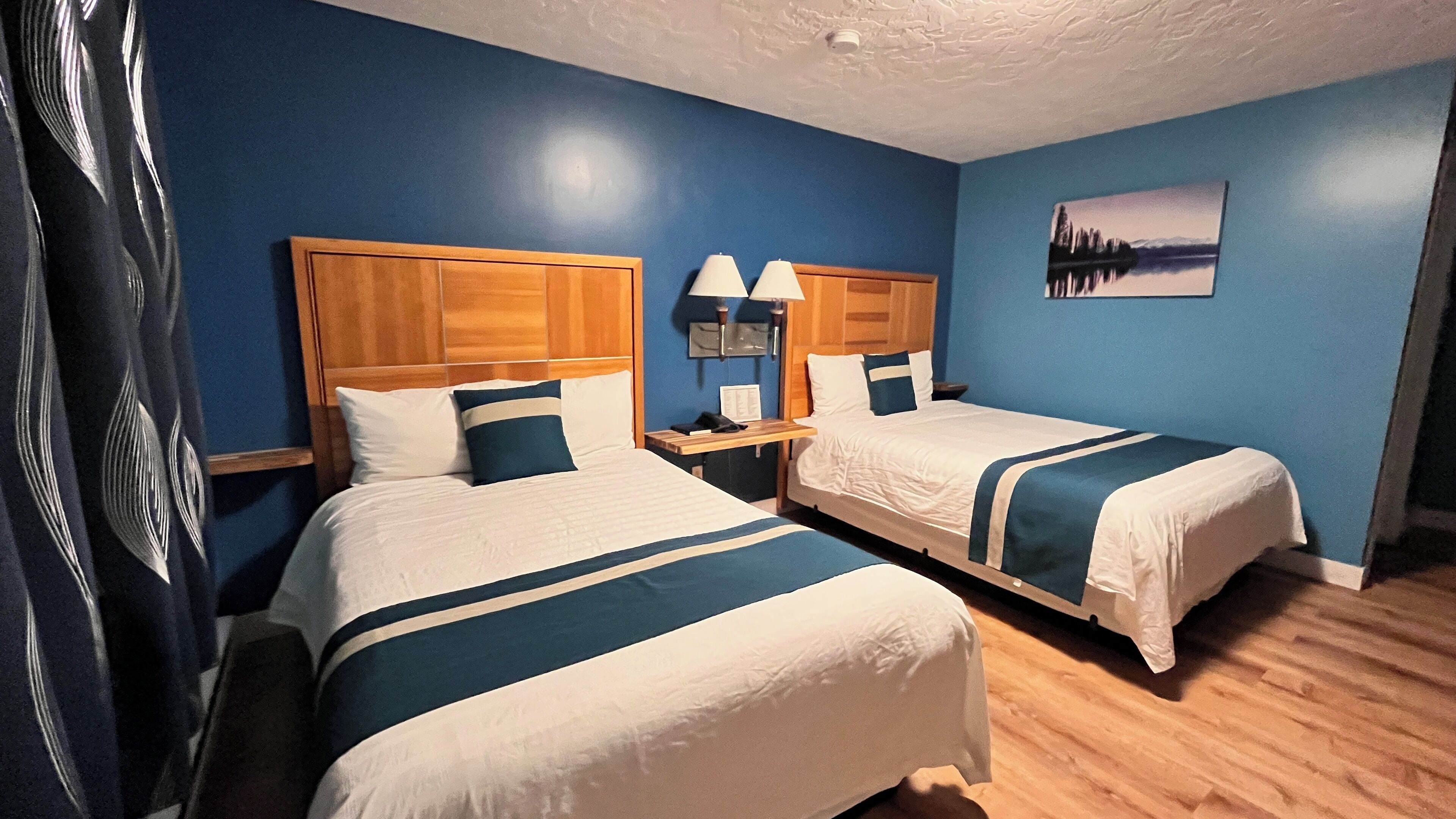 A hotel room with two beds, wooden headboards, and a blue wall.