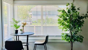 Una habitación de esquina con ventanal saliente, una mesa con dos sillas, una planta en maceta y un radiador.