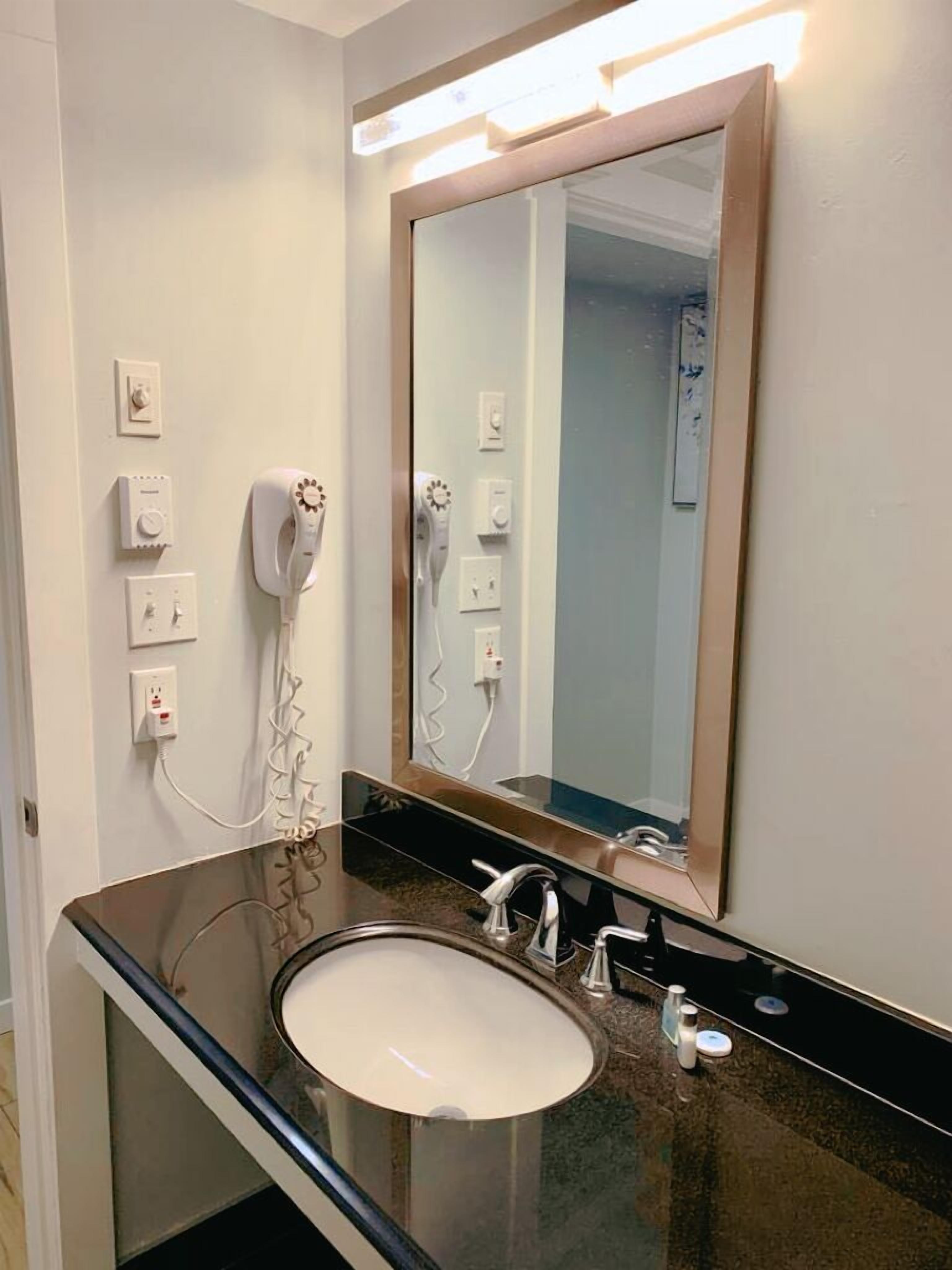 Een badkamer met een grote spiegel, een wastafel en een aan de muur bevestigde haardroger.