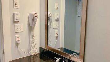 Un baño con un espejo grande, un lavabo y un secador de pelo montado en la pared.