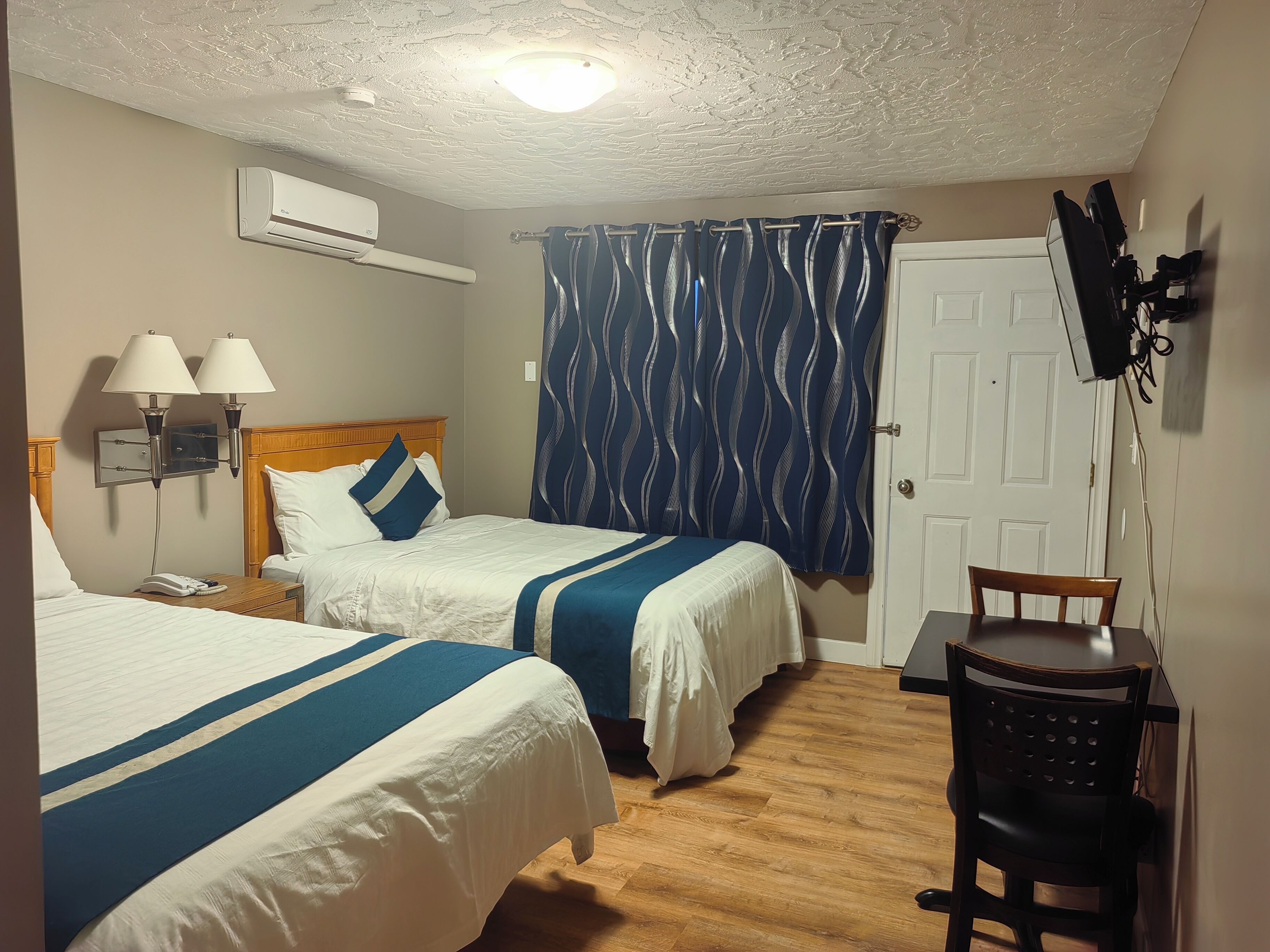Ein Hotelzimmer mit zwei Betten, einem Schreibtisch, einem Sessel, einem Fernseher und einer Klimaanlage.