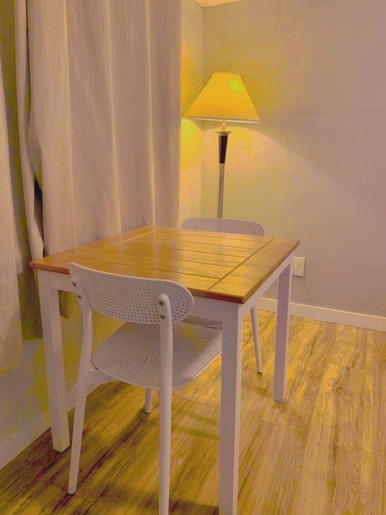 Ein Zimmer mit einem Holztisch, einem weißen Stuhl, einer Lampe und einem Vorhang.