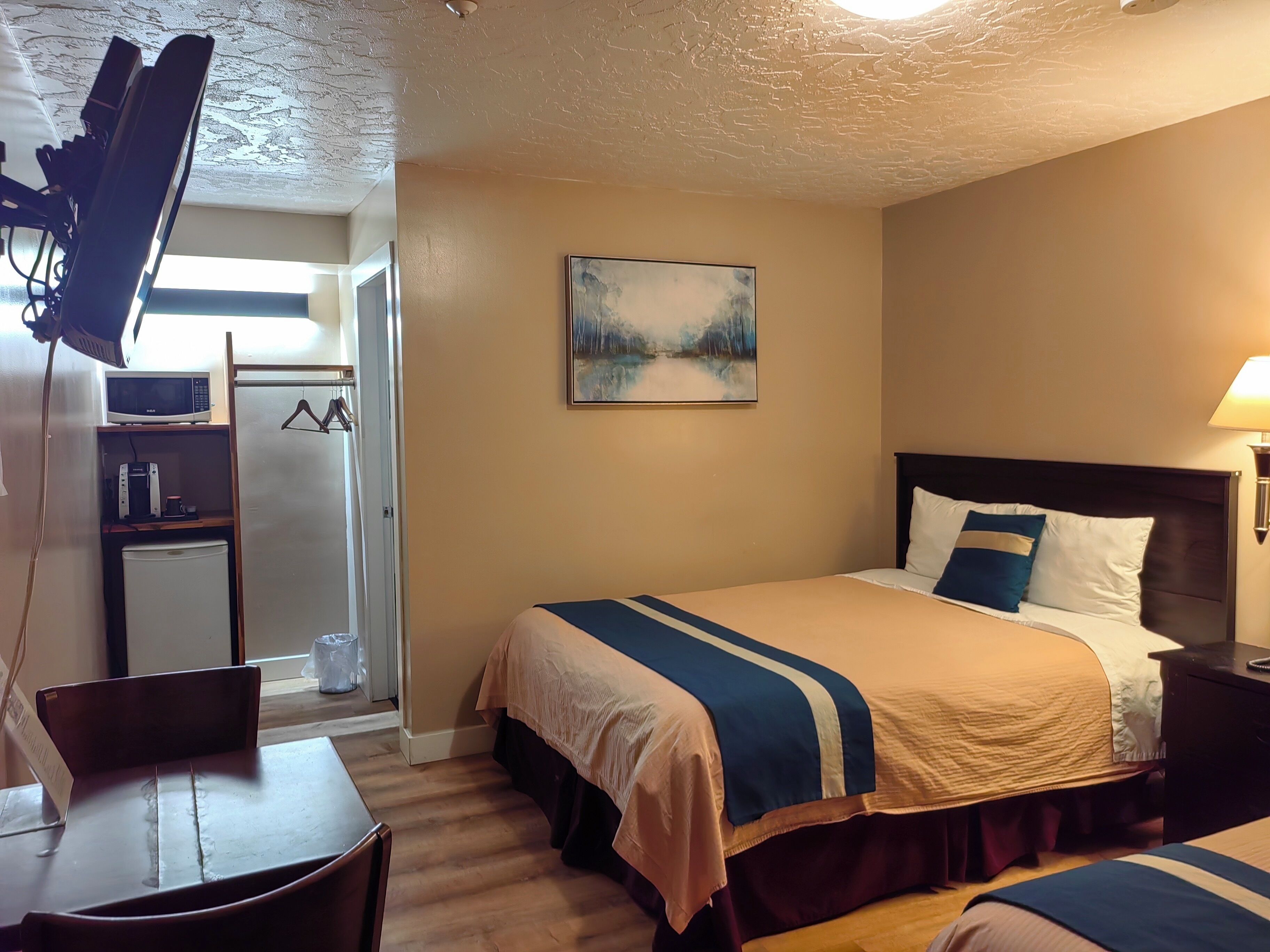Une chambre d’hôtel avec un lit, un bureau, un four à micro-ondes, un petit réfrigérateur, un tableau au mur et une lampe.