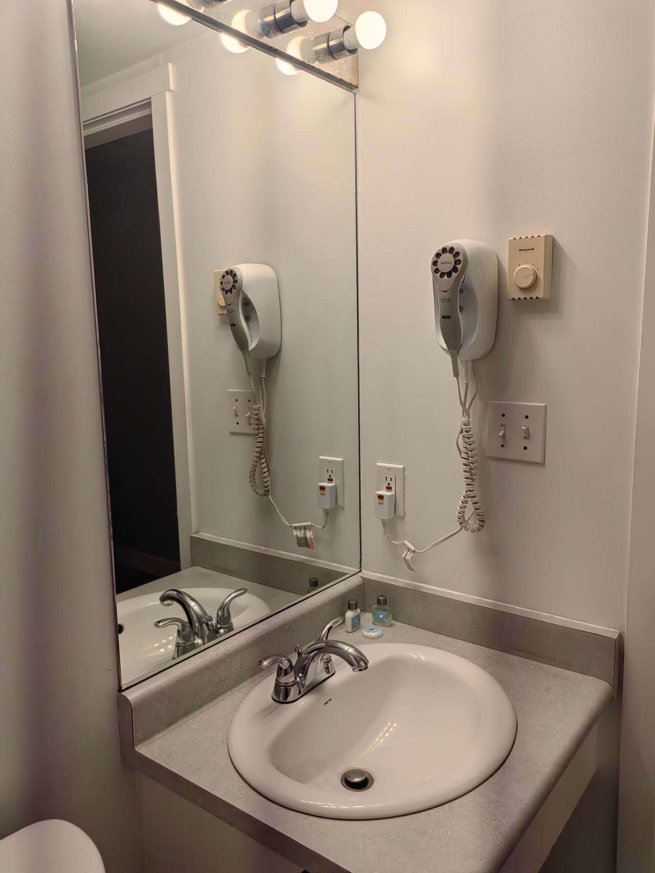 A bathroom with a sink, a mirror, and two hair dryers mounted on the wall.